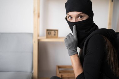 Siyah kar maskeli bir kadın hırsız kameraya bakıyor ve sessiz bir jest yapıyor. Maskeli kadın hırsız ev soygunu sırasında sessizlik işareti gösteriyor. Gizli suç faaliyeti kavramı.