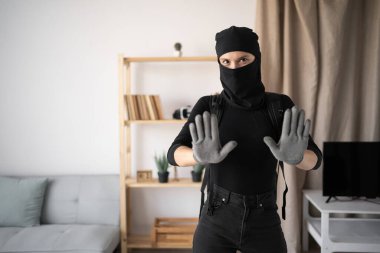 Siyah kar maskeli bir hırsız ya da soyguncu terörizm suçlusu evde para çalıyor, el kol hareketi yapıyor ve kameraya bakıyor. Boşluğu kopyala
