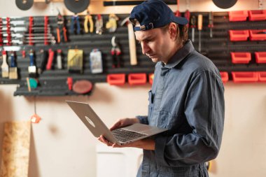 Dizüstü bilgisayarı olan bir marangoz. Marangozluk, marangozluk, atölyede proje uygulaması. Boşluğu kopyala