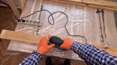 İlk bakışta turuncu koruyucu eldivenli erkek elleri zımpara makinesi kullanarak ahşap bir tahtayı zımparalıyor. Konsept: DIY hobi ve meşguliyet.