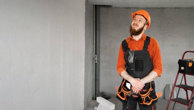 Sert şapkalı ve mavi tulumlu erkek sakallı müteahhit kemer üzerinde çalışırken gülümsüyor ve mesaj arıyor. Onarım, inşaat ve inşaat kavramı