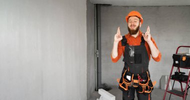 Sert şapkalı ve mavi tulumlu erkek sakallı müteahhit kemer takıp dilek diliyor. Onarım, inşaat ve inşaat kavramı