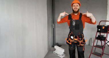 Kasklı ve mavi tulumlu erkek sakallı müteahhit kemeriyle kendini işaret ederek beni seçiyor. Onarım, inşaat ve inşaat konsepti