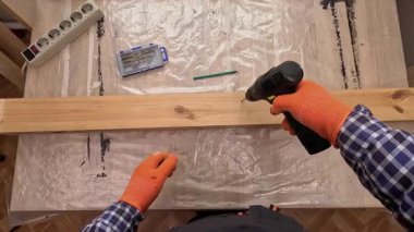 POV, kablosuz matkapla tahta bir tahtaya delik açan birini yakın plan çekiyor. Ahşap işleme, talaş ve DIY inşaat konsepti.