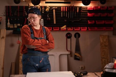 Kadın katılımcı atölye sahnesinde atölye kıyafetleri giyer. Duvarda asılı aletler çatışma ya da anlaşmazlık anında. Bayan marangoz gece geç saatlerde otantik garajda. Boşluğu kopyala