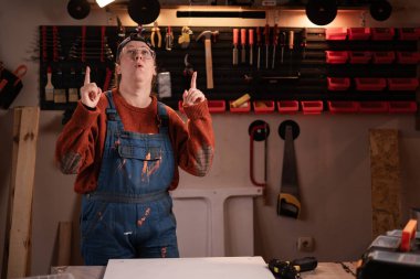 Çalışan kadın atölye sahnesinde atölye kıyafetleri giyiyor. Duvarda asılı aletler var. Bayan marangoz gece geç saatlerde otantik garajda. Boşluğu kopyala