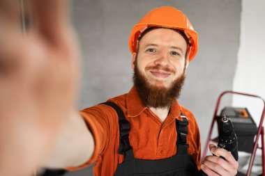 İnşaat işçisi sakallı adam inşaat alanında matkapla selfie çekiyor. Tamirci ev tamiri yapıyor. Profesyonel inşaatçı içeride. Boşluğu kopyala