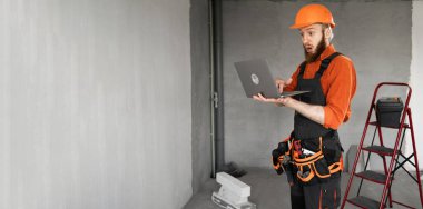 İnşaat işçisi sakallı adam inşaat alanında dizüstü bilgisayar kullanıyor. Tamirci ev tamiri yapıyor. Profesyonel müteahhit içeride. Boşluğu kopyala