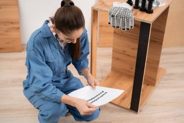 Kadın zanaatkar evde mobilya montajı yapıyor. Tamirci kadın işe başlamadan önce yükleme kılavuzunu okuyor. Tamirci mobilya montajı oturma odasında. Boşluğu kopyala