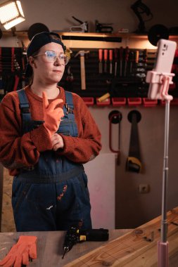 Marangoz kadın blogcu canlı yayın video blogunu ahşap atölyesinde akıllı telefon tripoduna kaydediyor. DIY blogcusu çalışıyor.