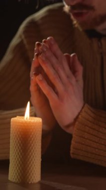 Yanan bir mumun yanında dua ederken katlanmış bir adamın elleri. Karanlık bir odada ruhanilik, inanç ve umut dolu bir atmosfer. Dini ritüel ve derin tefekkür.