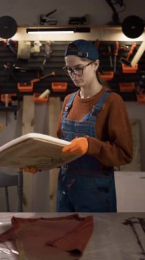 Tulumlu kadın tamirci köpük dolgu malzemelerini güncelleyerek ahşap sandalyeyi onarmaya hazırlanıyor. Mobilya restorasyonu, atölye çalışması. dikey video