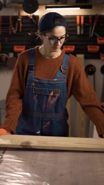 Kadın marangoz ya da işçi tulumuyla masaya tahta yığıyor. Ahşap işçiliği, marangozluk ve el işçiliği kavramı. Profesyonel bir zanaatkar yaratıcı atölyede kereste hazırlıyor..