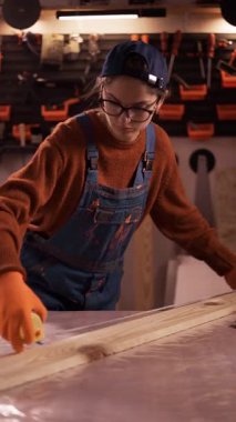 Dişi marangoz atölyede mezurayla tahta ölçü alıyor. Dikey video. Ahşap işçiliği, hassasiyet ve meslek anlayışı