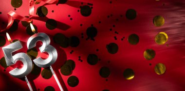 Doğum günü ve yıldönümü kutlaması kavramı. 53 numara 53 gümüş kutlayan doğum günü mumu büyük altın konfetiyle kırmızı arka planda. Elli üç yıllık doğum günü. düz yat.