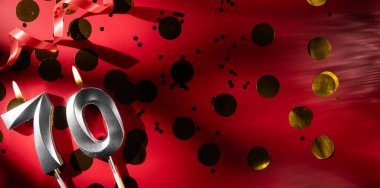 Doğum günü ve yıldönümü kutlaması kavramı. 70 numaralı doğum günü mumu, büyük altın konfetiyle kırmızı arka planda. 70 'inci yaş günü. düz yat