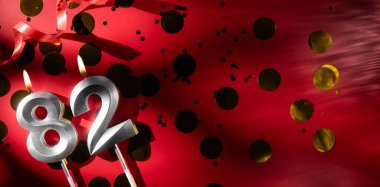 Doğum günü ve yıldönümü kutlaması kavramı. 82 numara, kırmızı arka planda büyük altın konfetiyle 82 numara, doğum günü mumu. Seksen iki yıllık doğum günü. düz yat