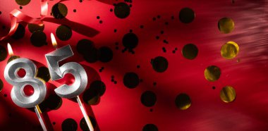 Doğum günü ve yıldönümü kutlaması kavramı. 85 numara 85 gümüş kutlayan kırmızı arka planda büyük altın konfetiyle doğum günü mumu. Seksen beş yıllık doğum günü. düz yat