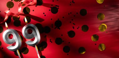 Doğum günü ve yıldönümü kutlaması kavramı. 99 numara, büyük altın konfetiyle şenlikli kırmızı arka planda 99 numara, doğum günü mumu. Doksan dokuz yıllık doğum günü. düz yat