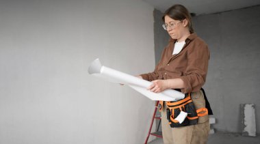 Alet kemeri olan odaklanmış bir kadın DIY ev yenileme projesinin kağıt planları üzerinde çalışıyor. Boşluğu kopyala