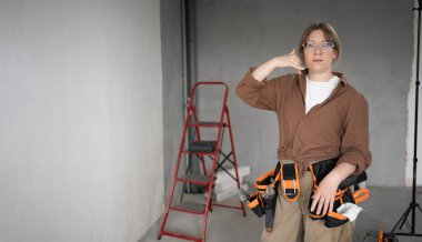 Alet kemeri takmış bir kadın ev tadilatı sırasında kameraya bakarak bana el hareketi yapıyor.