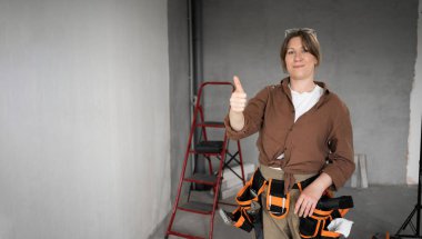 DIY ve ev geliştirme kavramı. Profesyonel bir alet kemeri takan bir kadın kameraya bakar ve onaylar, ev tadilatından ve apartman tadilatından memnuniyet duyar..