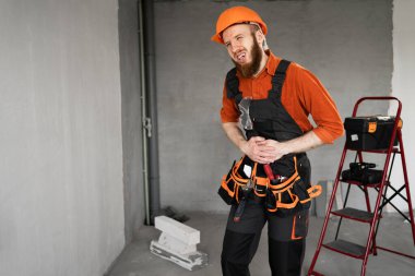 Mide ağrısı ve mide bulantısı çeken kasklı ve tulumlu hasta sakallı müteahhit. Tıp ve sağlık hizmetleri kavramı