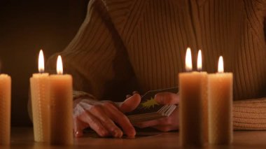 Gizemli erkek kahin karanlık odada yanıp sönen mum ışığında tarot kartı okuyor. Kehanet kavramı, manevi rehberlik ve okültizm yoluyla geleceği tahmin etme..