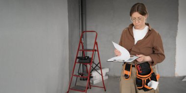 İşçi kadın, alet kemeri okuma projesi takıyor ve yeni evde plan yapıyor. Yenileme dairesi. Ev konseptini onar