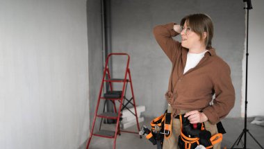 Stresli tamirci kadın alet kemeri takıyor. Yeni evde sol tarafa bakıyor. Yenileme dairesi. Evi ve duygu konseptini onar