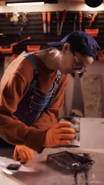 Kadın tamirci atölyedeki plastik tepsiye siyah boya döküyor. El işi, yenileme ve ev geliştirme konsepti. dikey video