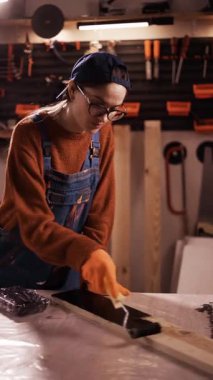 Profesyonel kadın marangoz, tahta tahtayı siyah boya pateniyle boyuyor. Ahşap işçiliği, mobilya restorasyonu ve DIY konsepti. dikey video