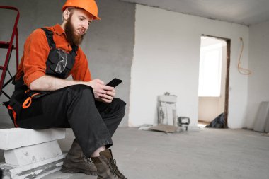 İnşaat işçisi, endüstriyel binadaki bir cep telefonunda dinlenme sohbetinin keyfini çıkarıyor. Boşluğu kopyala