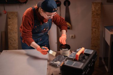 El sanatları ve DIY el yapımı. Kadın, marangozluk atölyesindeki boya fırçasıyla ahşap mobilya parçaları boyuyor. Boşluğu kopyala