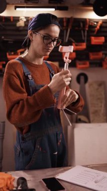 Becerikli kadın etkileyicisi, aboneler için video dersi kaydetmek için telefon kamerası ve tripod kuruyor. Otantik atölyenin içinden canlı yayın yapan kadın tamirci. dikey video