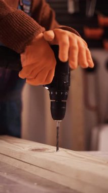 Turuncu eldivenli marangoz elleri ahşap kalaslarda delik açıyor. Marangozluk atölyesinde tahta delme işlemi. dikey video