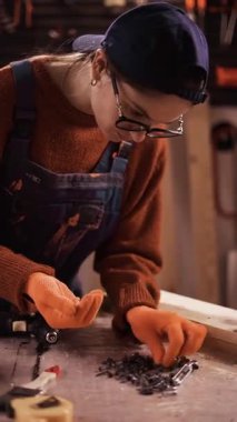 Marangozluk atölyesinde montaj için metal mobilyaları inceleyen gözlüklü kadın marangoz. dikey video