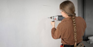 Alet kemeri takan odaklanmış bir kadın elektrikli çekiç matkabıyla duvarda bir delik açıyor, daireyi yeniliyor. Pankart. Boşluğu kopyala