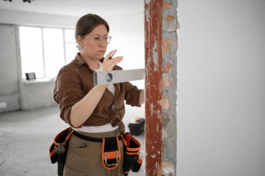 Kadın işçi, yenilenme sırasında ruh seviyesini kullanarak duvarı ölçüyor. Boşluğu kopyala