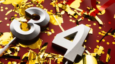 Kırmızı bayramda konfeti arkaplanlı 34 numaralı doğum günü rakamı. 34 'üncü yaş günü. Doğum günü, yıldönümü ve tarih kavramı. yakın plan