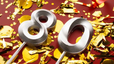 80 numaralı kırmızı şenlik kutlamasında konfeti arka planında. Seksen yıllık doğum günü. Doğum günü, yıldönümü ve tarih kavramı. Boşluğu kopyala