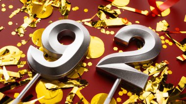 Kırmızı bayramda konfeti arkaplanlı 92 numaralı doğum günü rakamı. Doksan iki yaş günü. Doğum günü, yıldönümü ve tarih kavramı. Boşluğu kopyala