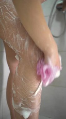 Bacağını banyo süngeriyle yıkayan kadının yakın çekimi. Dikey video