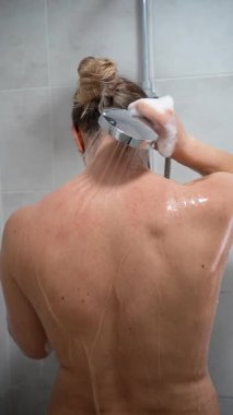 Duşun altındaki kadın, sırtına akan su. Kişisel bakım konsepti. Yakın plan. Dikey video