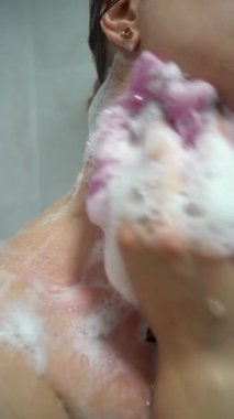 Güzellik ve vücut bakımı konsepti. Kadın vücudu sünger kullanarak yıkıyor, banyoda boynu ovuyor. dikey video