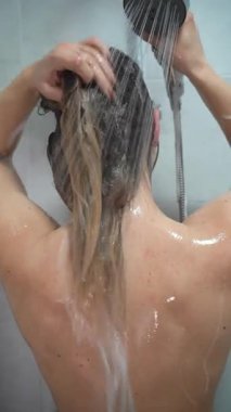 Duşta saçını yıkayan kadının arkası, yakın plan. Dikey video