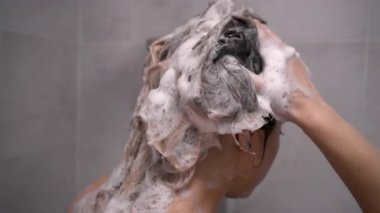 Kadın saçını şampuan köpüğüyle yıkıyor. Cilt bakımı ve kişisel hijyen konsepti. Boşluğu kopyala