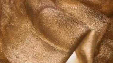 Parlayan altın parıldayan dudak parlatıcısının kozmetik dokusu metal spatulayla karışır. Güzellik kozmetik ürünleri için arka plan. yakın plan