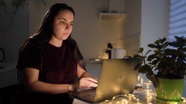 Pijamalı yorgun bir kadın dizüstü bilgisayarın önünde esniyor, gece geç saatlere kadar mutfakta çalışıyor. Boşluğu kopyala