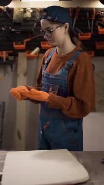 Bir kadın ustabaşı atölyede turuncu koruyucu eldivenlerini çıkartıyor. İş sağlığı ve güvenliği kavramı ve fiziksel iş gücü gerektiren mesleki eğitim.